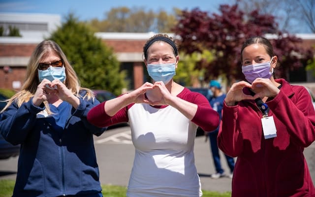 Trois membres du personnel hospitalier côte à côte et faisant un signe "coeur" avec leurs mains